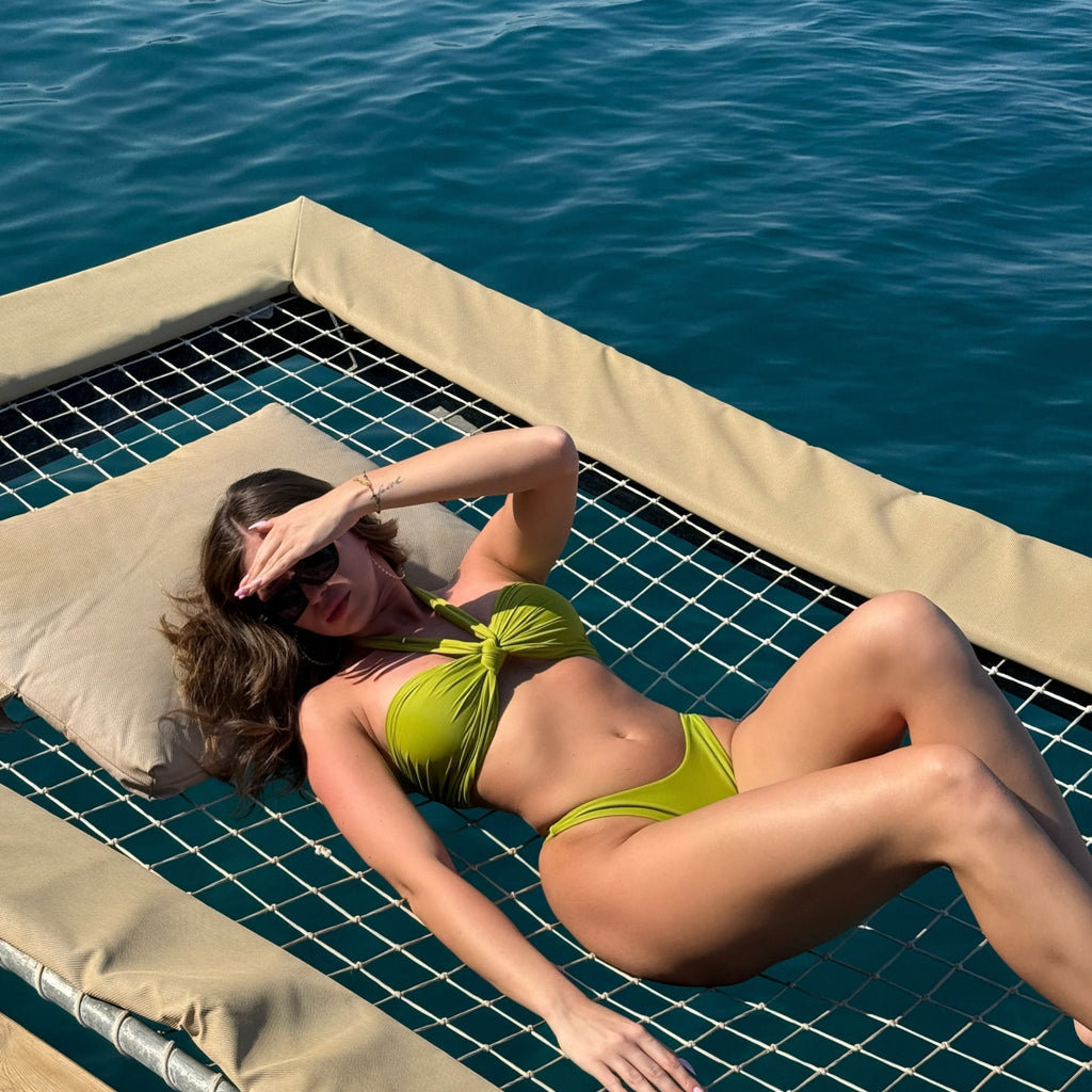 brunette woman in green bikini sunbathing on deck by water brunette woman in green bikini sunbathing on deck by water