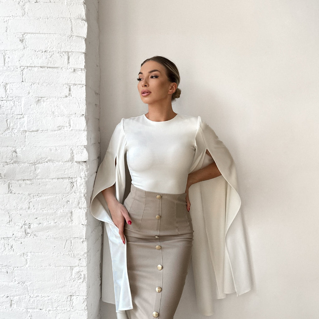 woman in white blouse and beige skirt standing near white wall woman in white blouse and beige skirt standing near white wall
