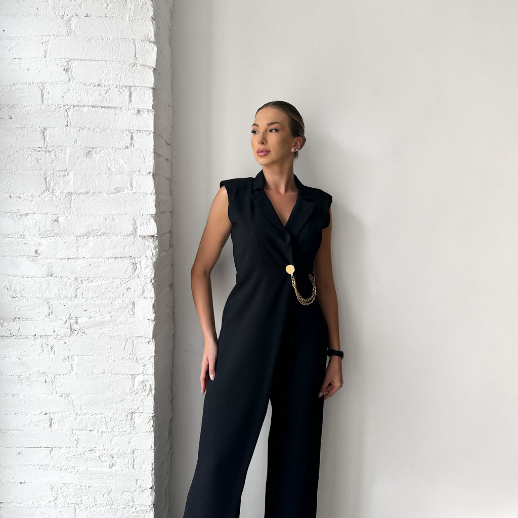 woman wearing black jumpsuit with chain belt standing against white brick wall woman wearing black jumpsuit with chain belt standing against white brick wall