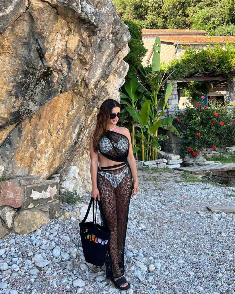 woman wearing black sheer beach dress holding a bag on rocky shore woman wearing black sheer beach dress holding a bag on rocky shore