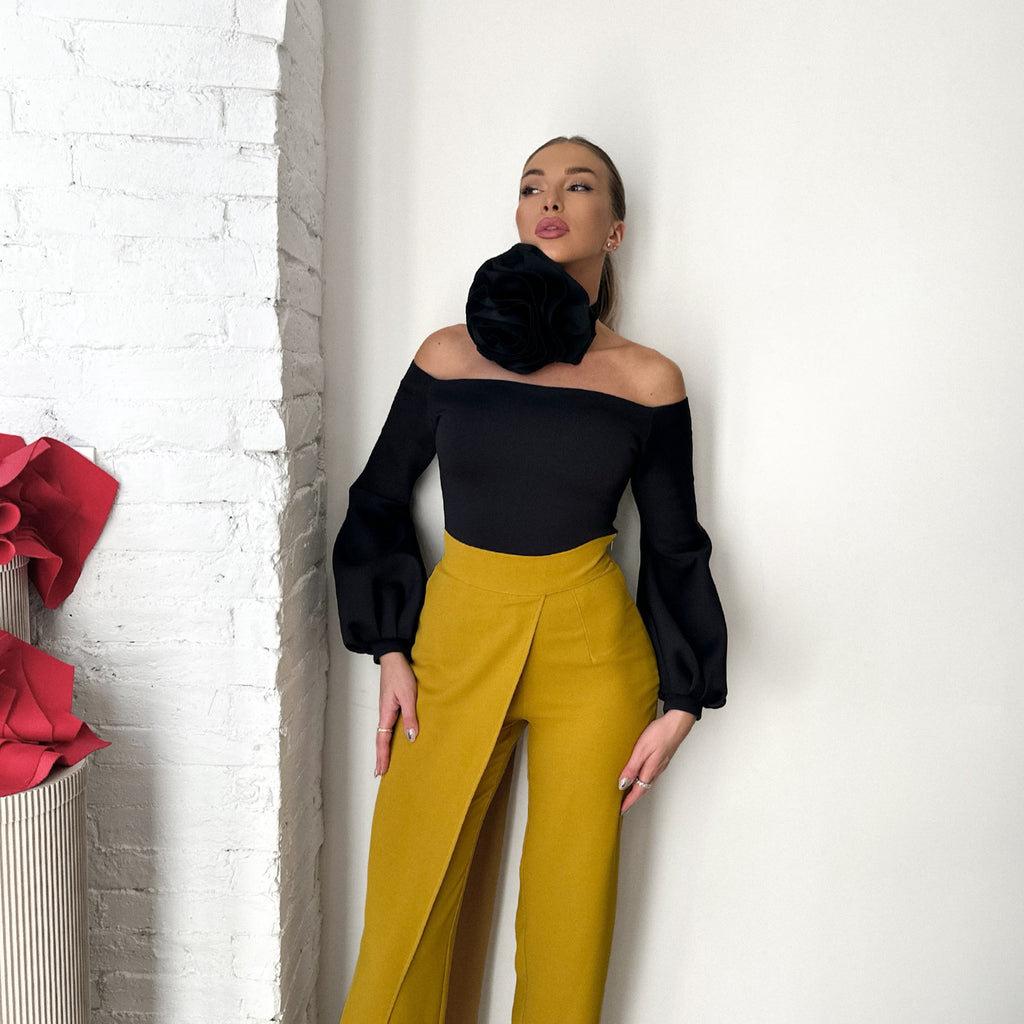 woman in black top and yellow pants standing against white wall woman in black top and yellow pants standing against white wall