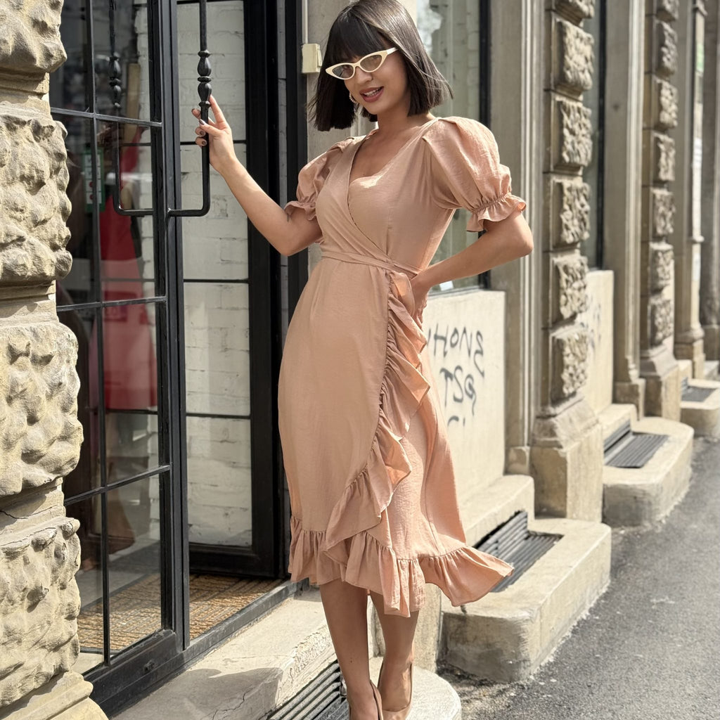 woman in peach wrap dress with ruffle details and cat eye glasses standing outside urban building woman in peach wrap dress with ruffle details and cat eye glasses standing outside urban building