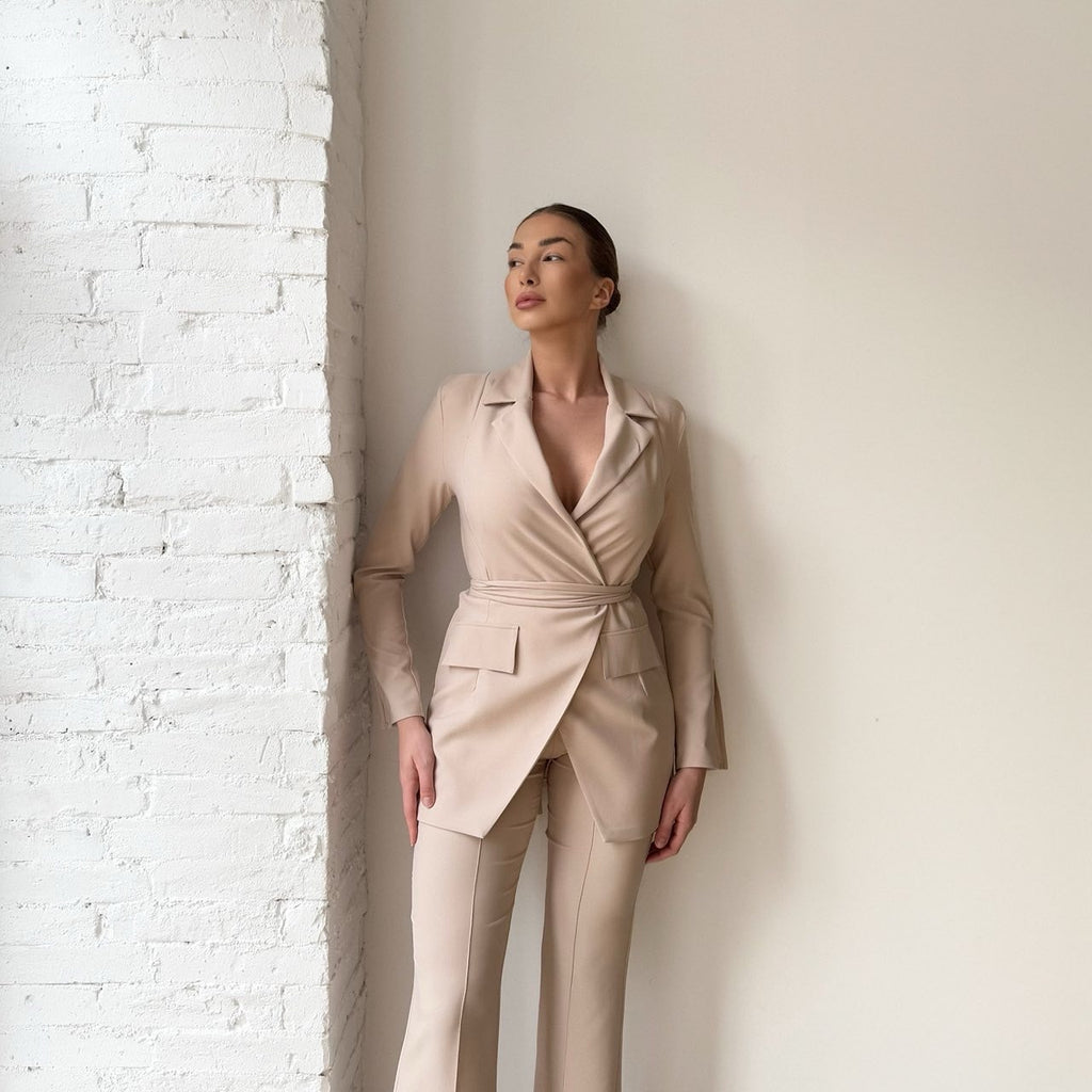 beige suit woman standing near white brick wall beige suit woman standing near white brick wall