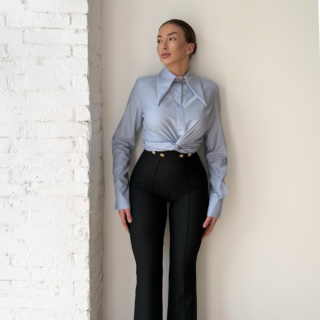 woman in blue shirt and black trousers standing against white wall woman in blue shirt and black trousers standing against white wall