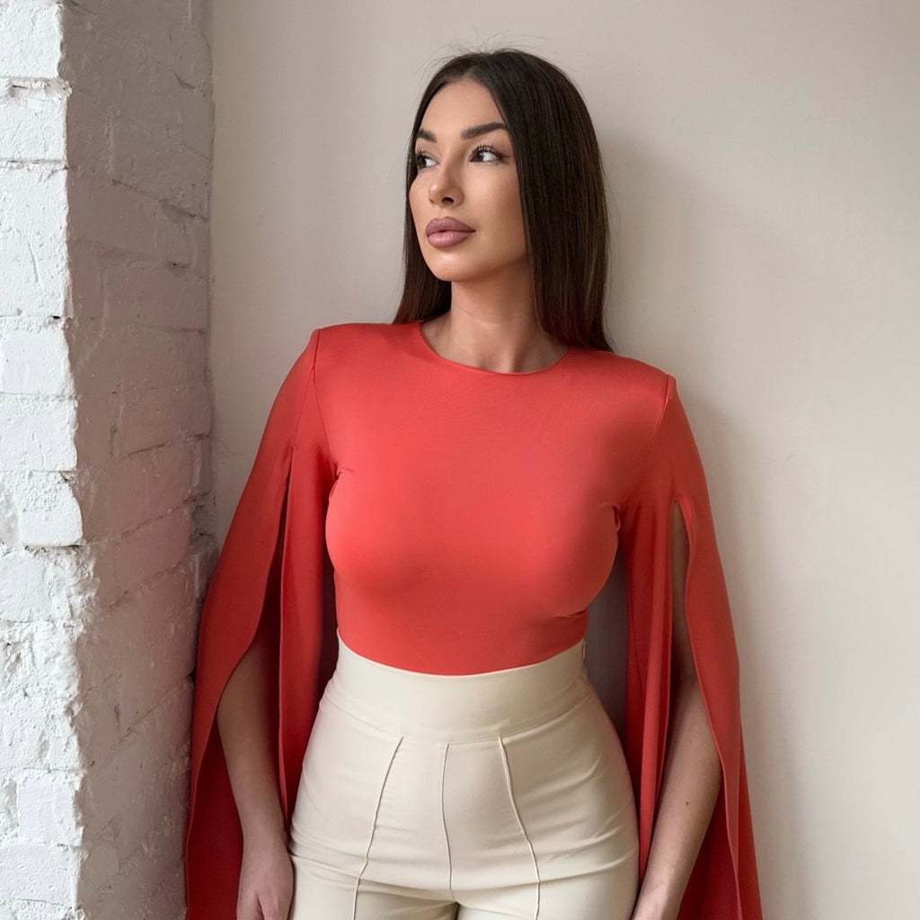 woman in orange cape top and white high waisted pants woman in orange cape top and white high waisted pants