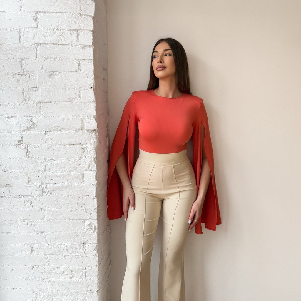 bright orange top with cream pants near white brick wall bright orange top with cream pants near white brick wall