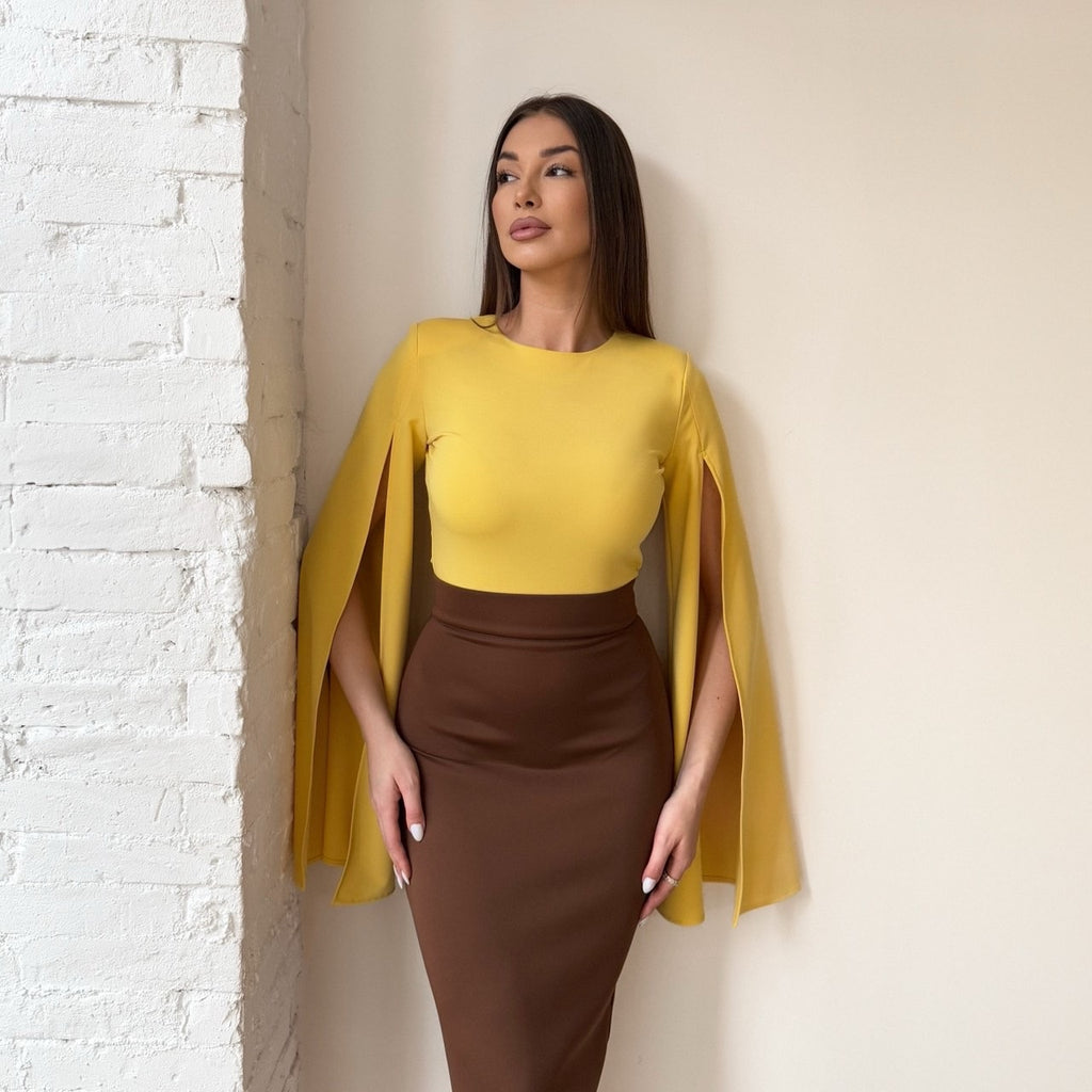 woman in yellow and brown dress standing against white brick wall woman in yellow and brown dress standing against white brick wall