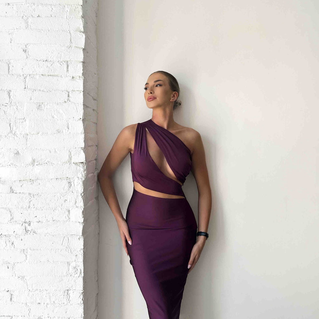 woman wearing purple one shoulder cutout dress standing against white wall woman wearing purple one shoulder cutout dress standing against white wall