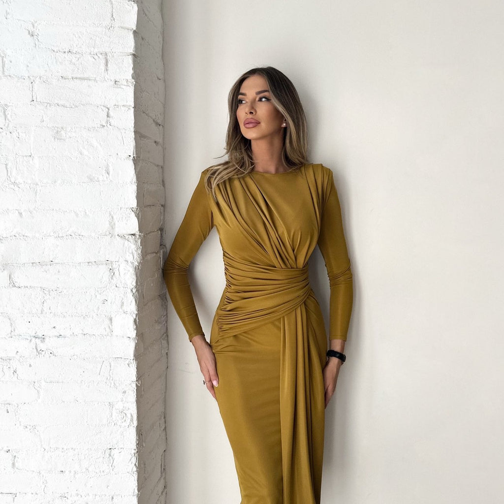woman in mustard draped dress leaning on white brick wall woman in mustard draped dress leaning on white brick wall