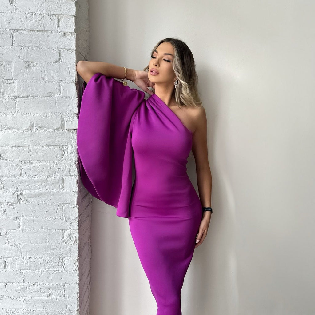 woman in purple one shoulder dress standing against white wall woman in purple one shoulder dress standing against white wall