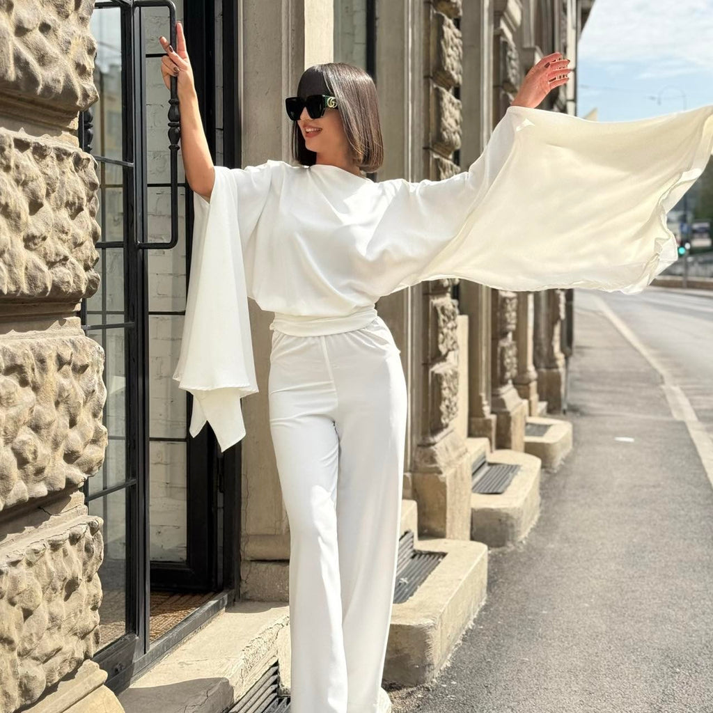 woman in elegant white outfit with wide sleeves and green shoes standing outside woman in elegant white outfit with wide sleeves and green shoes standing outside