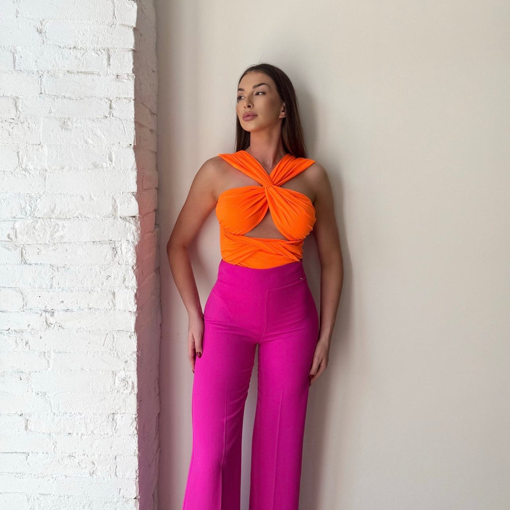 woman in orange top and pink pants standing against white brick wall woman in orange top and pink pants standing against white brick wall