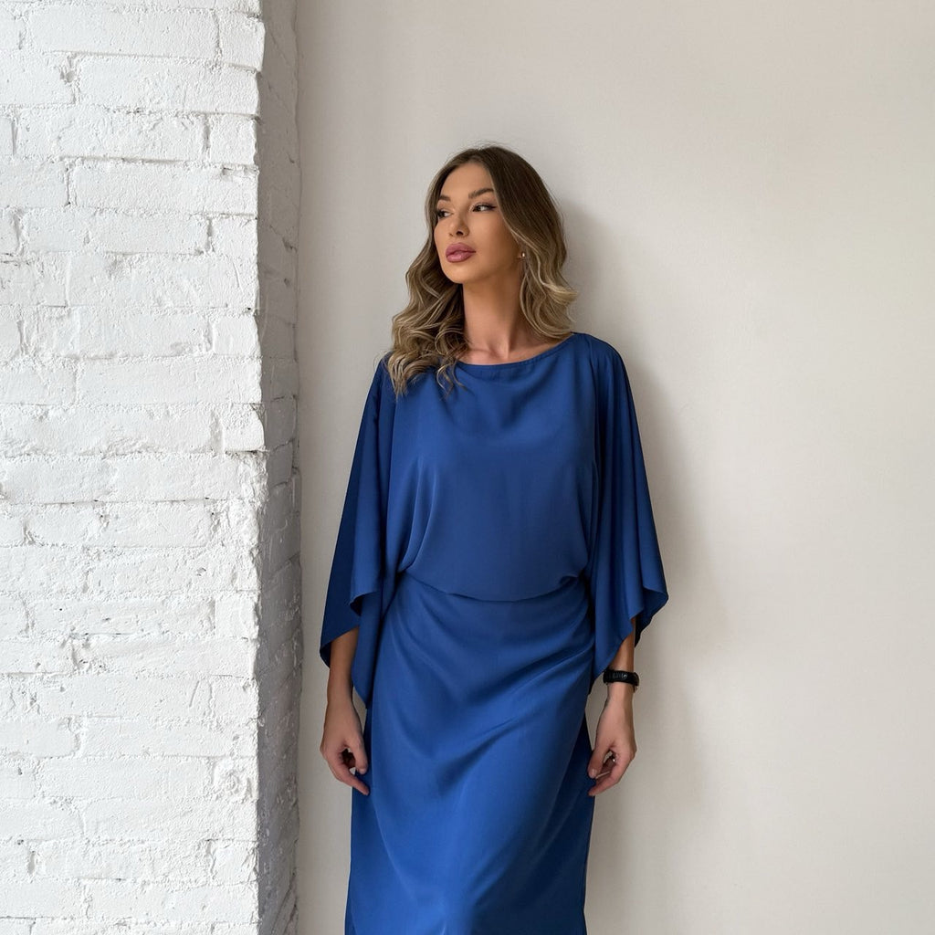 woman in blue dress standing against white brick wall woman in blue dress standing against white brick wall