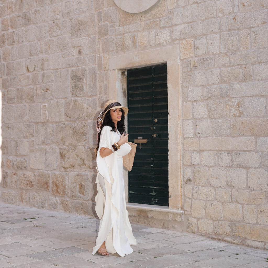 woman in white dress with hat and bag standing near stone wall woman in white dress with hat and bag standing near stone wall
