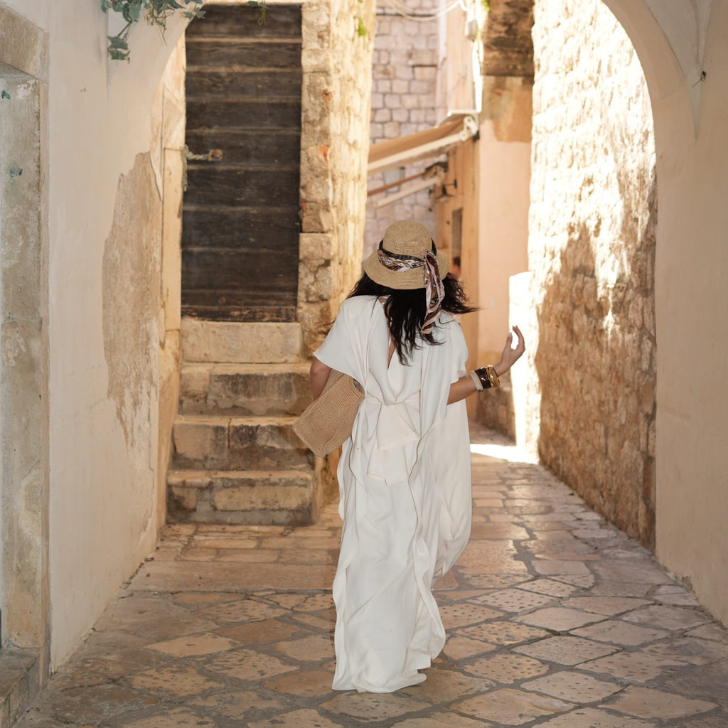 woman in white dress and sun hat walking through stone archway woman in white dress and sun hat walking through stone archway