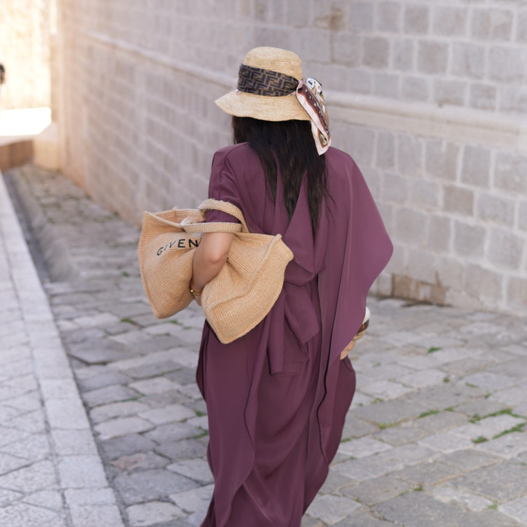 woman in purple dress with straw hat and bag on stone pathway woman in purple dress with straw hat and bag on stone pathway
