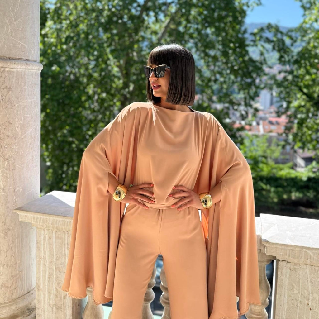 woman in peach cape jumpsuit wearing sunglasses posing outdoors woman in peach cape jumpsuit wearing sunglasses posing outdoors