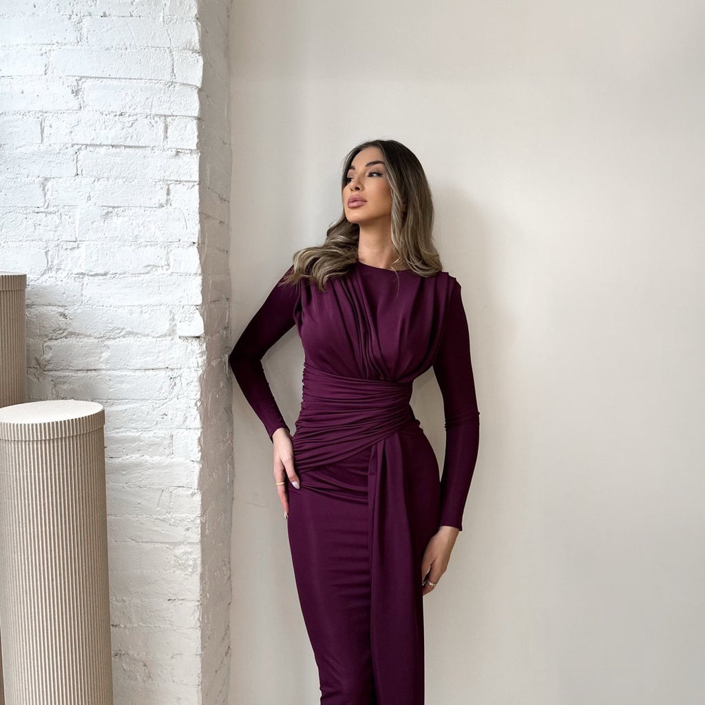 woman in maroon dress standing against white wall woman in maroon dress standing against white wall