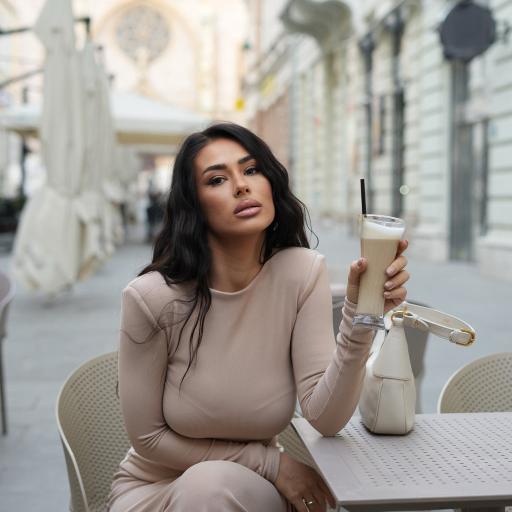 woman in beige maxi dress sitting at outdoor cafe table holding iced coffee woman in beige maxi dress sitting at outdoor cafe table holding iced coffee