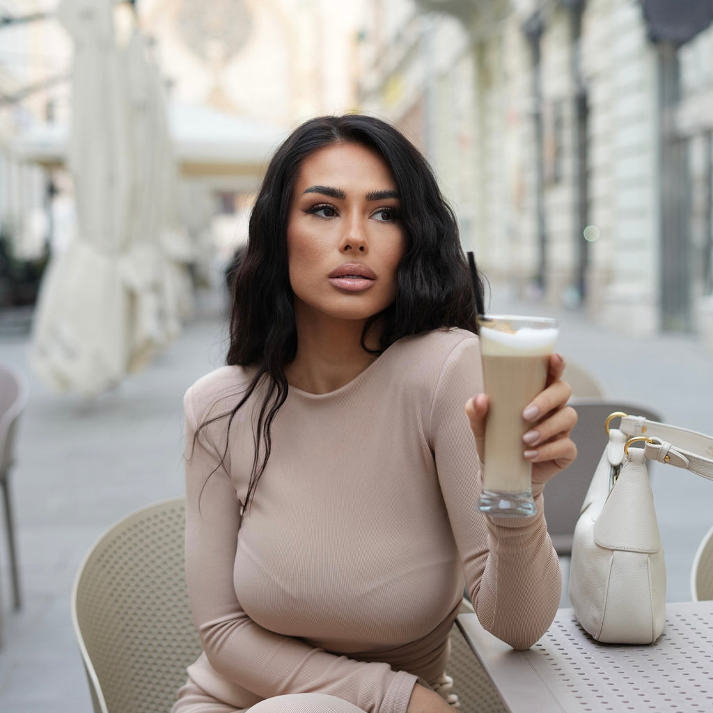 woman in beige dress holding latte at outdoor cafe woman in beige dress holding latte at outdoor cafe