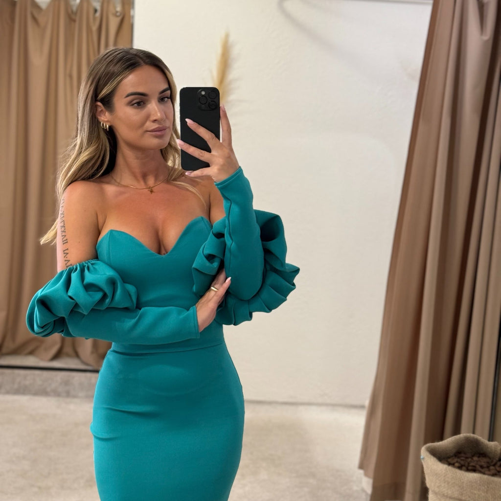 woman in teal ruffled sleeve dress taking selfie in dressing room woman in teal ruffled sleeve dress taking selfie in dressing room