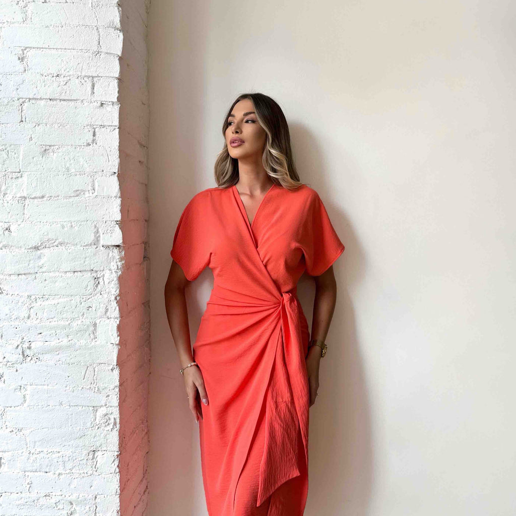 model wearing orange wrap dress against brick wall model wearing orange wrap dress against brick wall