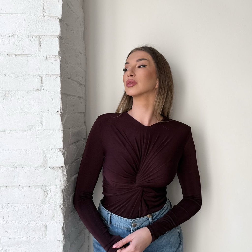 woman wearing burgundy long sleeve top and blue jeans standing by white wall woman wearing burgundy long sleeve top and blue jeans standing by white wall
