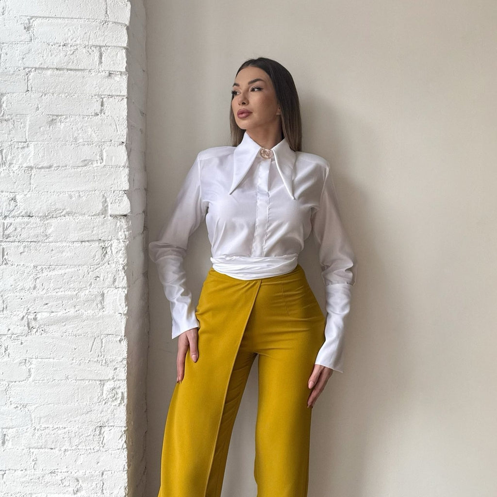 woman in white shirt and yellow pants standing near white brick wall woman in white shirt and yellow pants standing near white brick wall