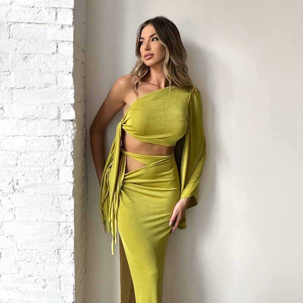 model wearing one shoulder olive green dress standing against white wall model wearing one shoulder olive green dress standing against white wall