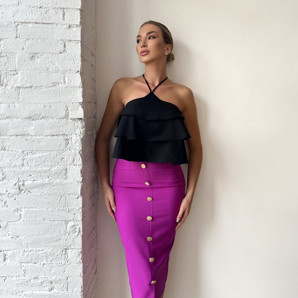 woman in black ruffle top and pink buttoned skirt standing against white wall woman in black ruffle top and pink buttoned skirt standing against white wall