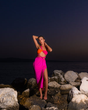 woman in bright pink and orange dress on rocky beach at dusk