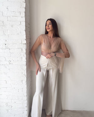 woman wearing beige top and white pants standing by brick wall