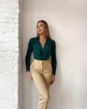 woman in teal top and beige pants standing against white brick wall