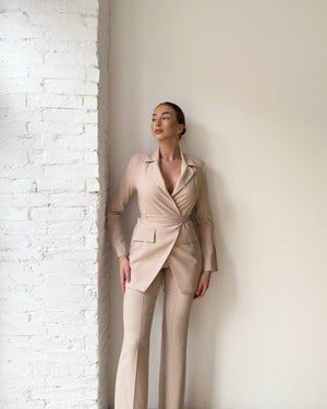 beige suit woman standing near white brick wall