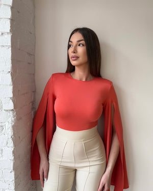 woman in orange cape top and white high waisted pants