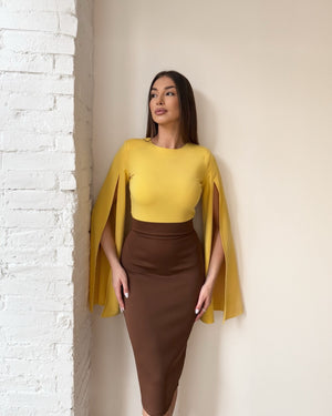 woman in yellow and brown dress standing against white brick wall