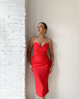 woman in red strapless midi dress standing against white wall