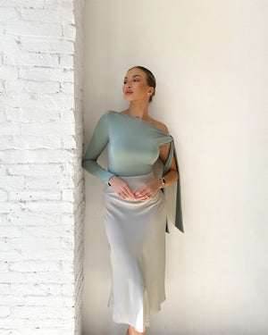 elegant woman in one shoulder dress leaning against white wall