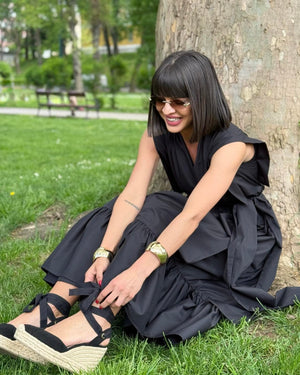 woman sitting in a park wearing black dress and sandals
