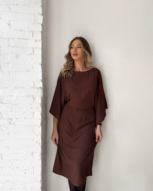 woman wearing brown midi dress against white brick wall
