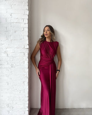 elegant woman in burgundy evening gown leaning on white wall