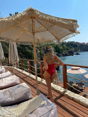 blonde woman in red swimsuit under umbrella near seaside