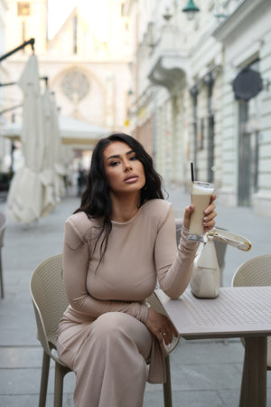 woman in beige maxi dress sitting at outdoor cafe table holding iced coffee