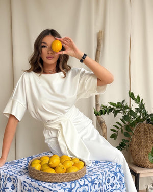model in white dress holding lemon near face