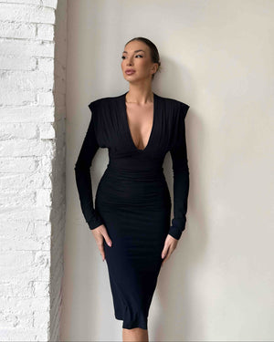 woman in black long sleeve dress standing against white wall