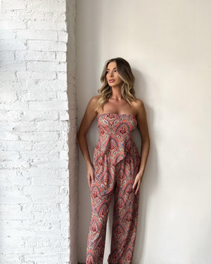 woman wearing strapless patterned jumpsuit standing by white brick wall