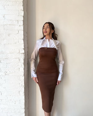 woman wearing brown dress over white shirt standing against a wall